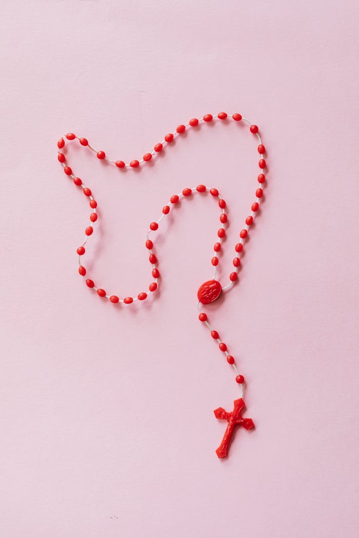 Red rosary beads on a soft pink background symbolizing faith and spirituality.