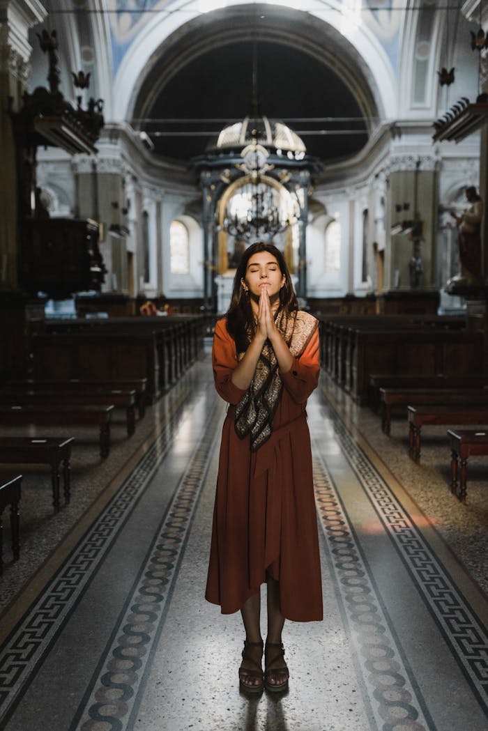 A woman stands praying in a beautifully lit historic church interior.